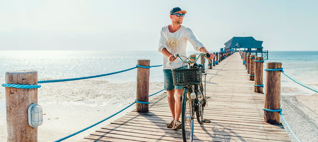 Chico paseando en bicicleta por una pasarela de playa con el mar de fondo